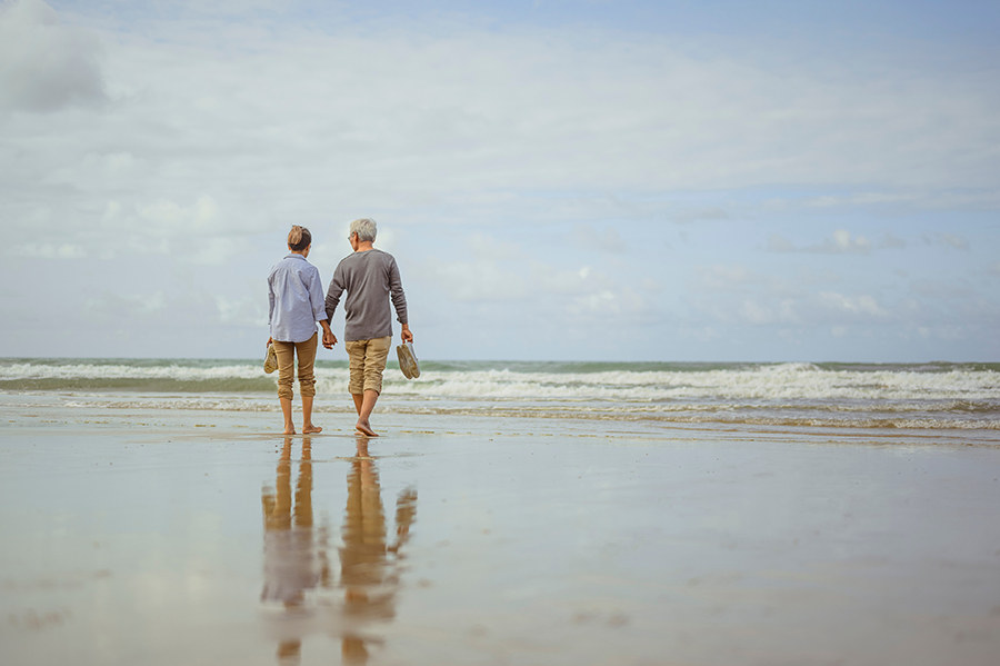 Senior couple walking on the beach holding hands at sunrise, plan life insurance at retirement concept
